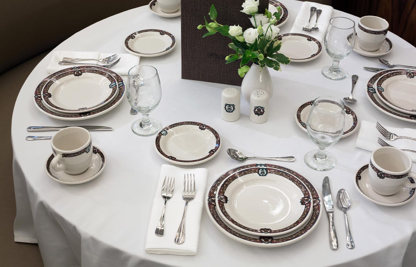 A table set for five with white linens and fine china and accompanying cutlery around a white floral centerpiece 