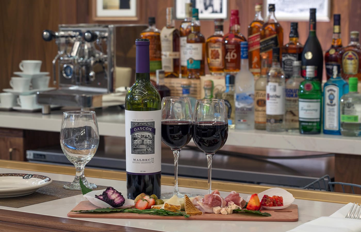 Wine and cheese pairing set atop a bar top showcasing a variety of spirits in the background