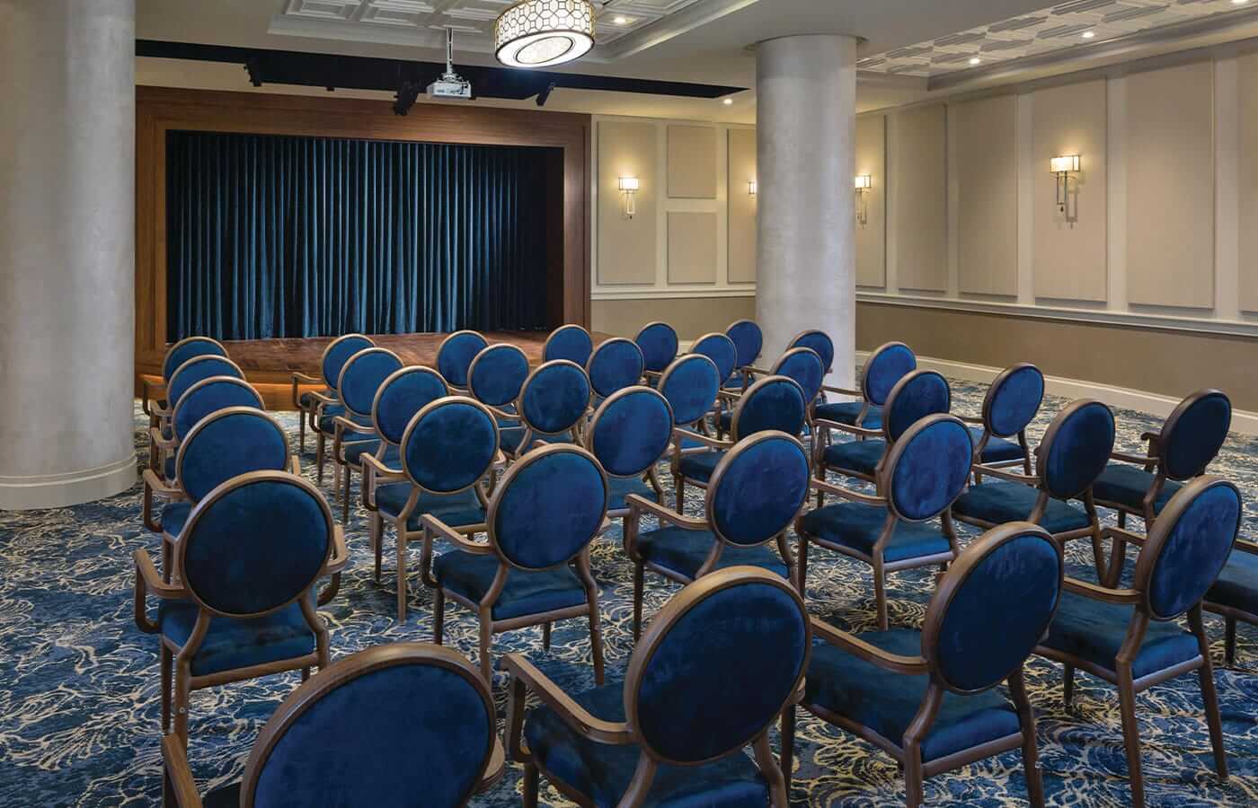 A look inside the performance centre at the Watermark at Brooklyn Heights featuring blue velvet backed chairs and blue velvet curtains adorning a mahogany stage