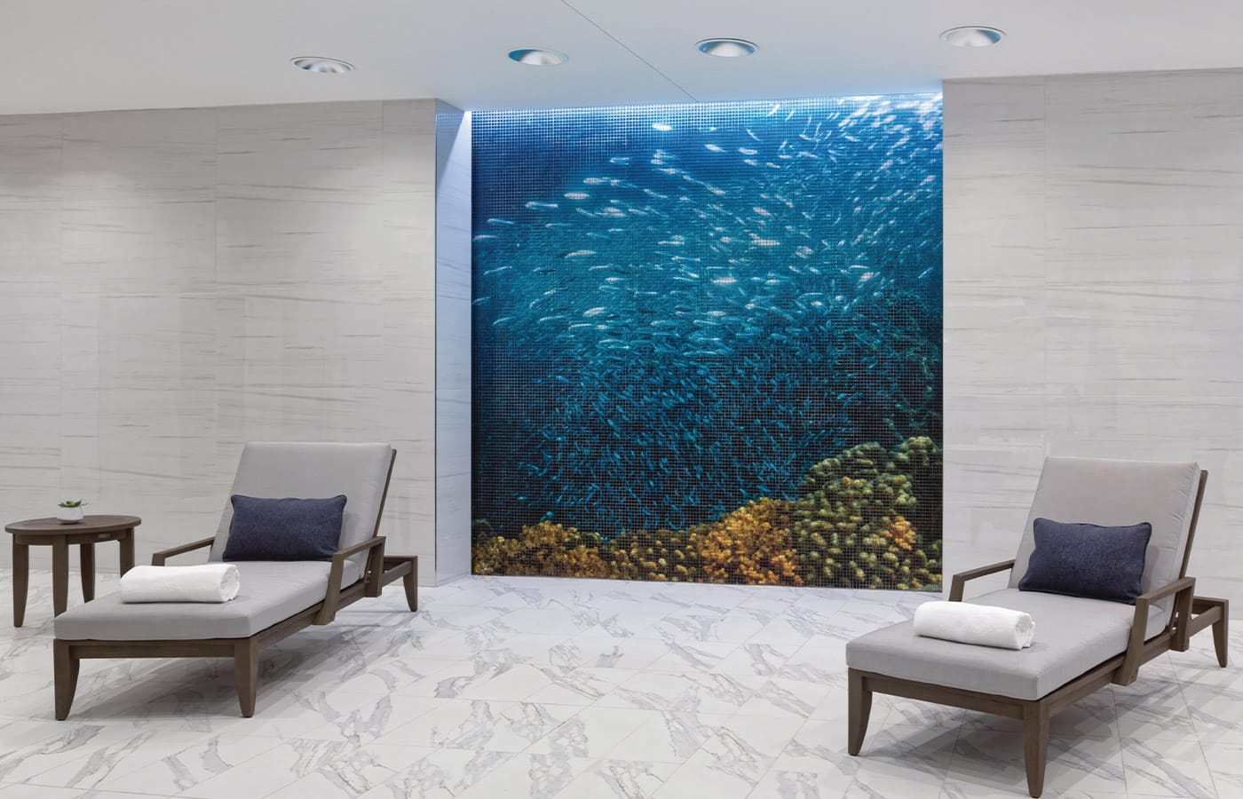 Lounge chairs found at the indoor pool space placed in front of a mosaic mural depicting the view from the sea floor looking upwards