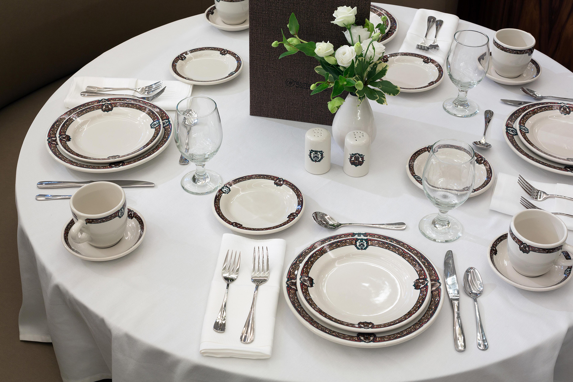 Dinner plates and cutlery set around a floral centrepiece atop a white table cloth