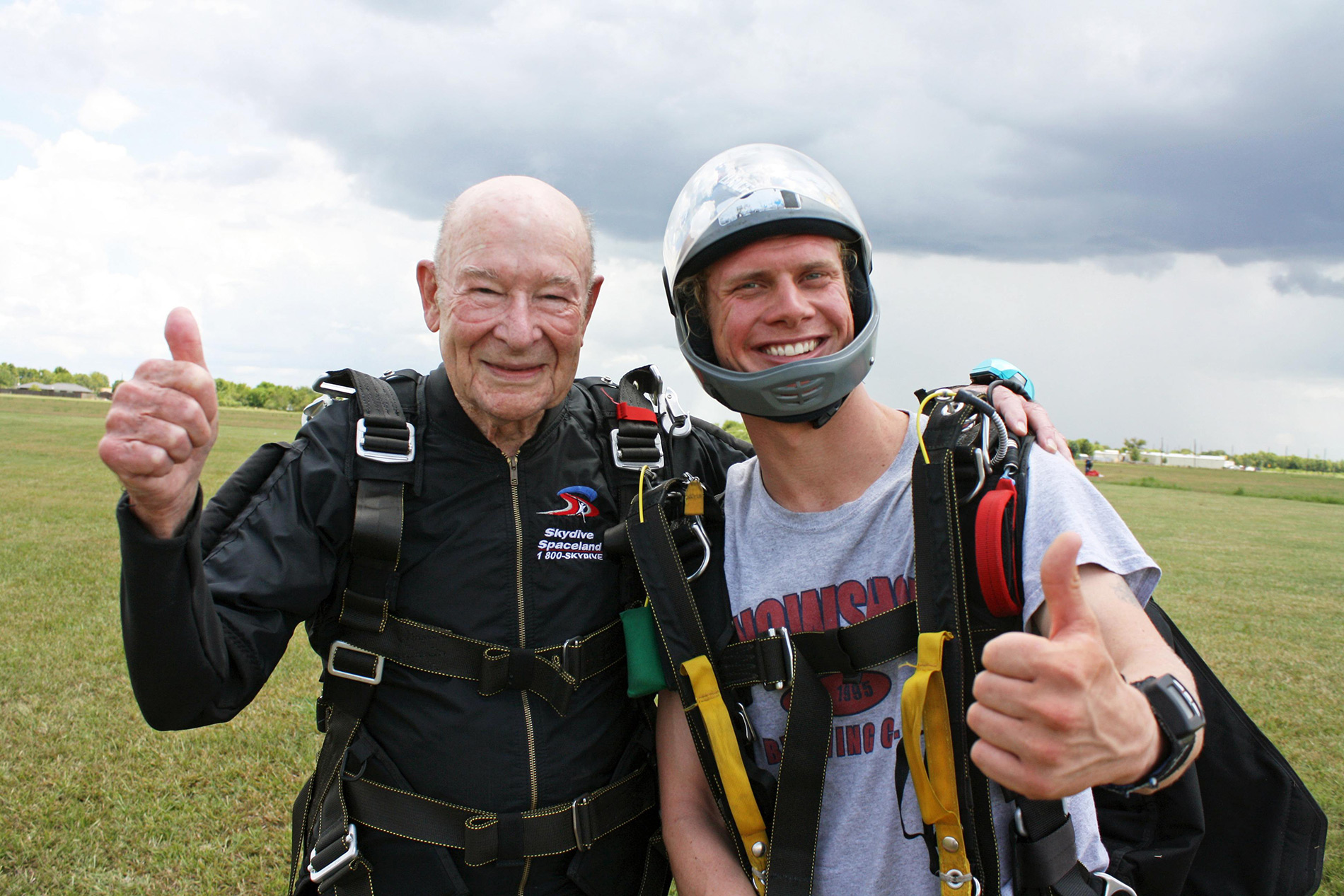 elderly gentleman and his son standing in a field in skydiving gear
