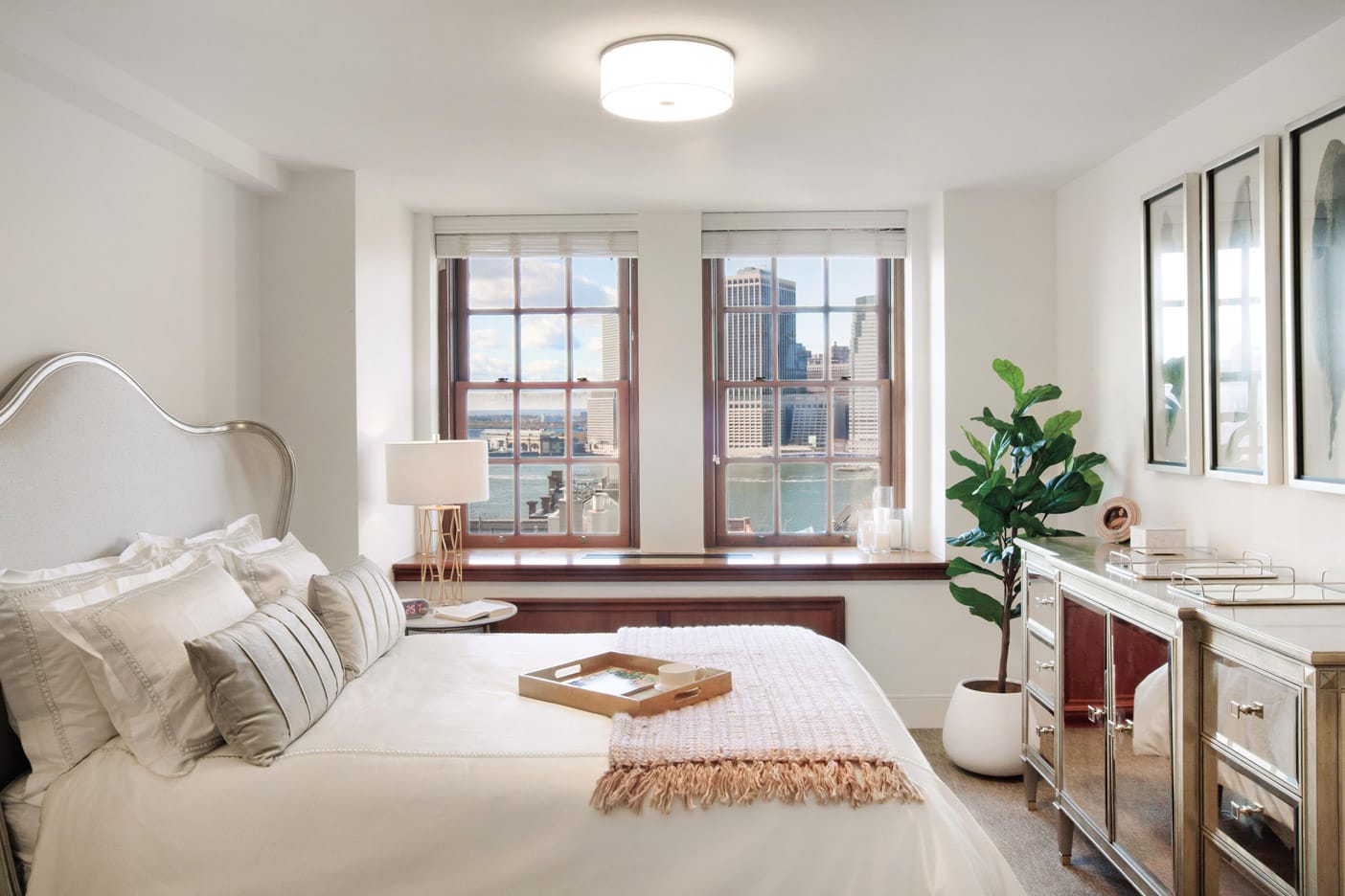 Brooklyn Heights Independent & Assisted Living Photo Gallery - Bedroom layout showcasing a neatly made bed, dresser, seating area, and a view of New York through mahogany framed windows
