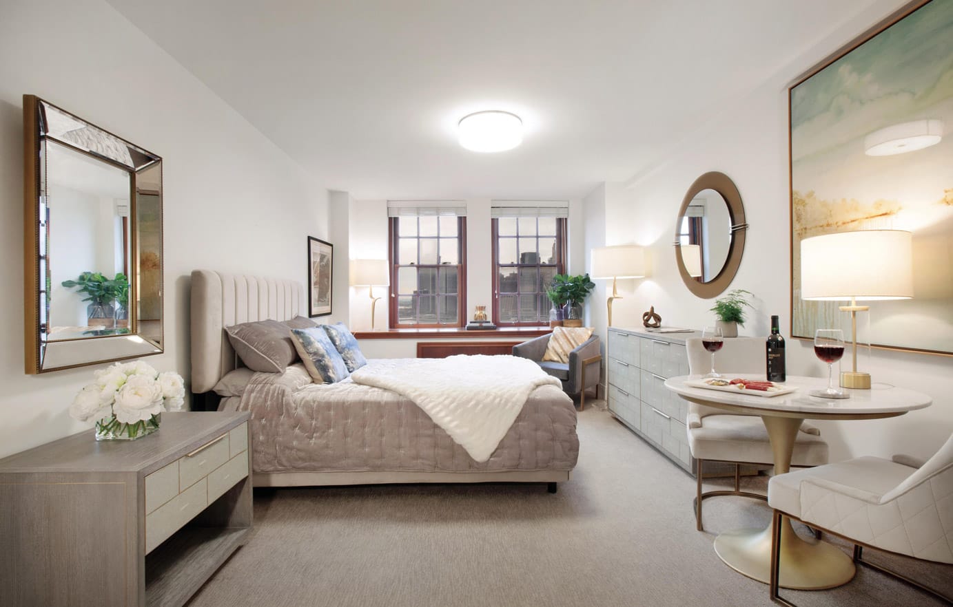 Brooklyn Heights Independent & Assisted Living Photo Gallery - bedroom layout featuring an elongated night stand, a dresser, a seating area, and a view of New York through the mahogany framed windows