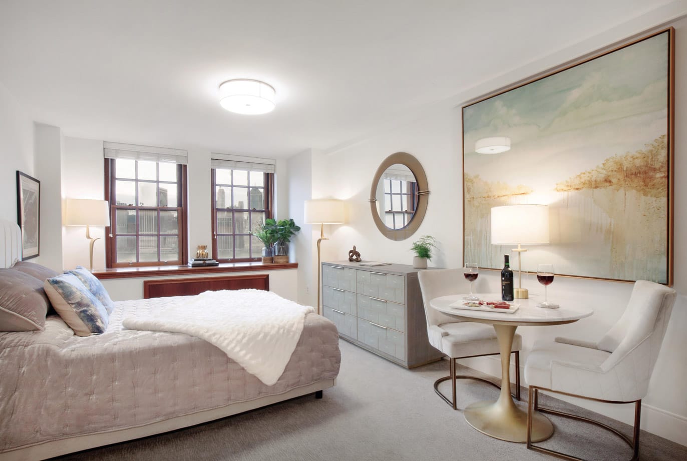 Brooklyn Heights Independent & Assisted Living Photo Gallery - bedroom layout featuring an elongated night stand, a dresser, a seating area, and a view of New York through the mahogany framed windows