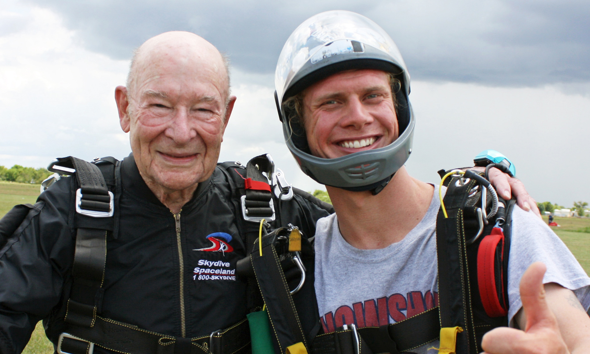 elderly gentleman and his son standing in a field wearing skydiving gear