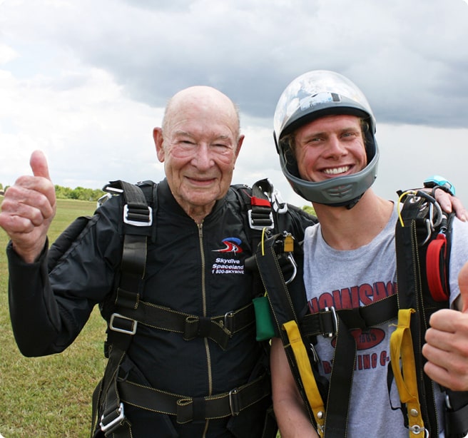 elderly gentleman and his son standing in a field wearing skydiving gear