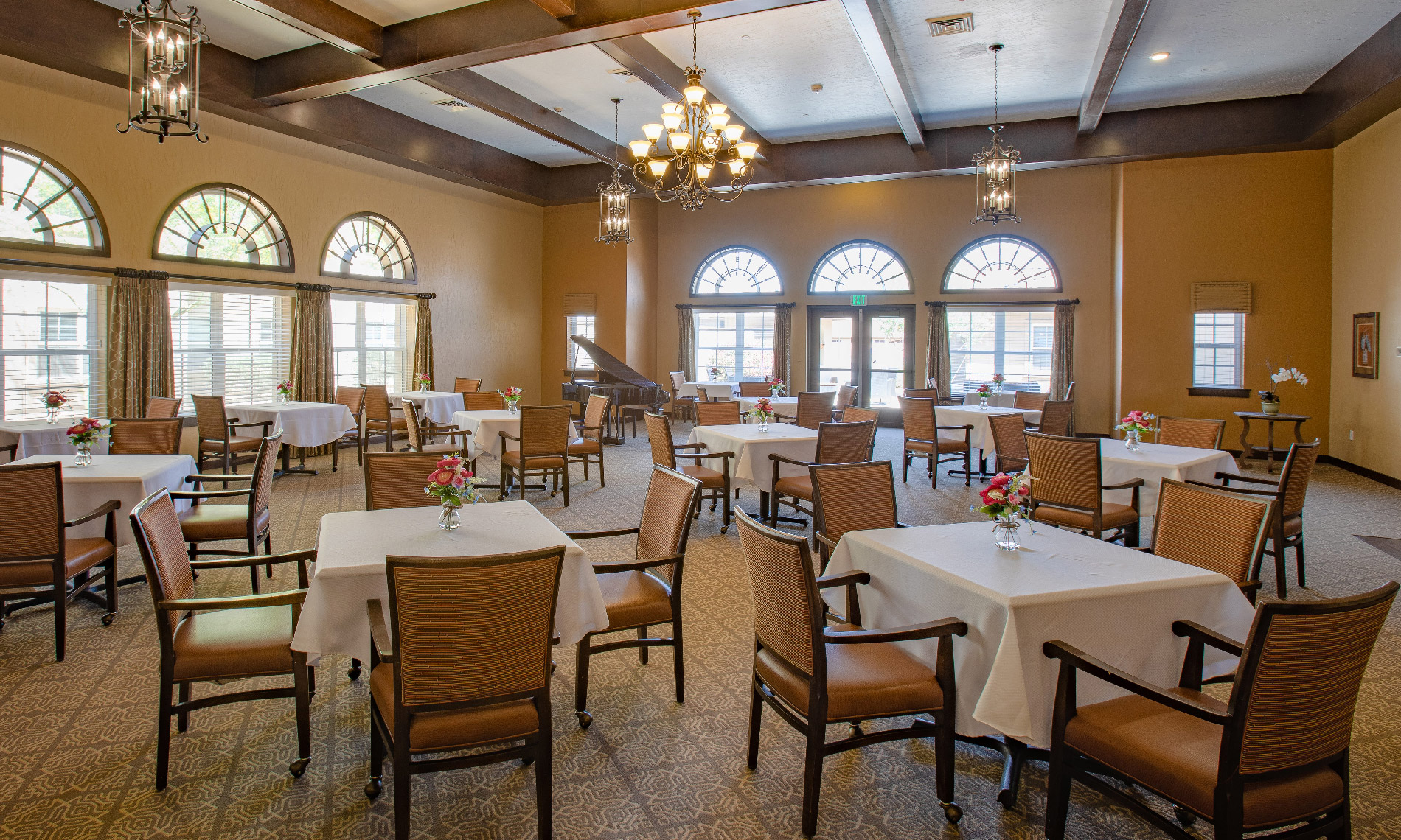A bright overview of the entire dinning room. All tables are set with White tablecloths, in the back of the room a grand piano can also be observed 