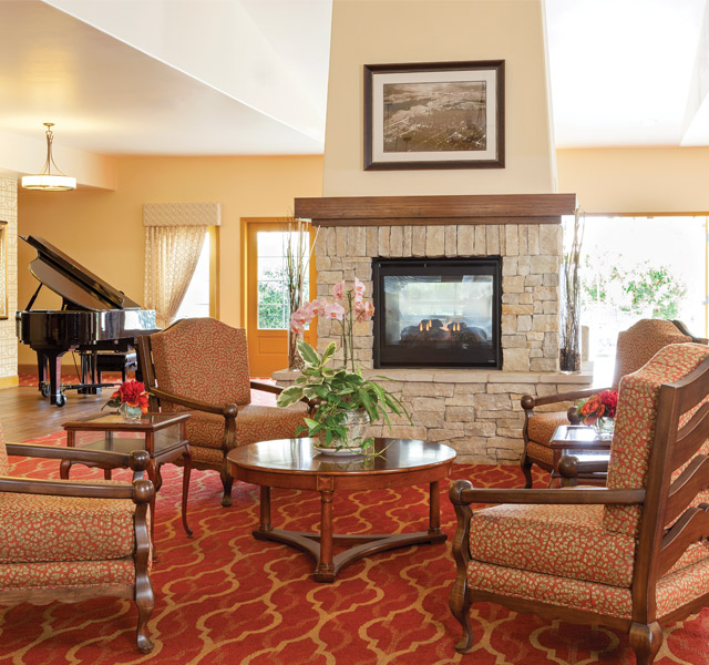 Hall with armchair, fireplace and a grand piano in the back by the bright windows