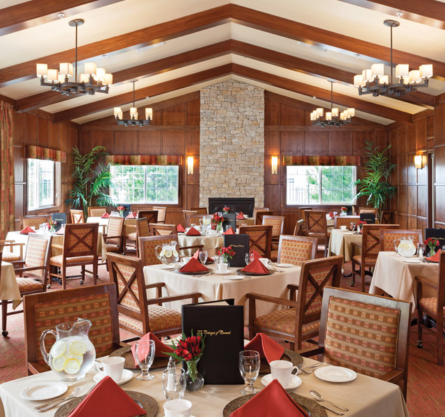 A large dining room with all table elegantly setup and large open window across the room 