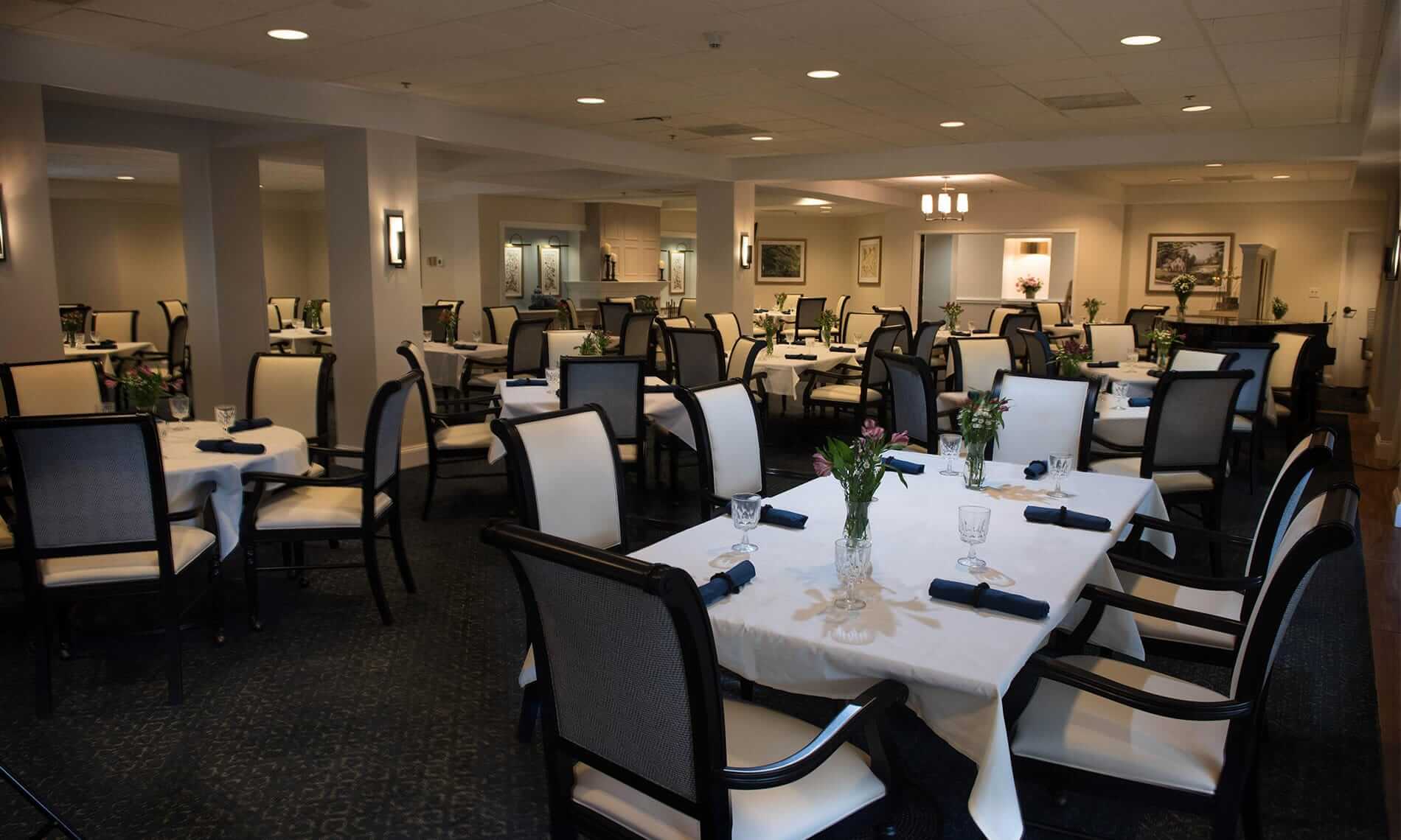 A dining room featuring tables with white linen table clothes, blue napkins, and high back chairs at the Fountains at the Albemarle