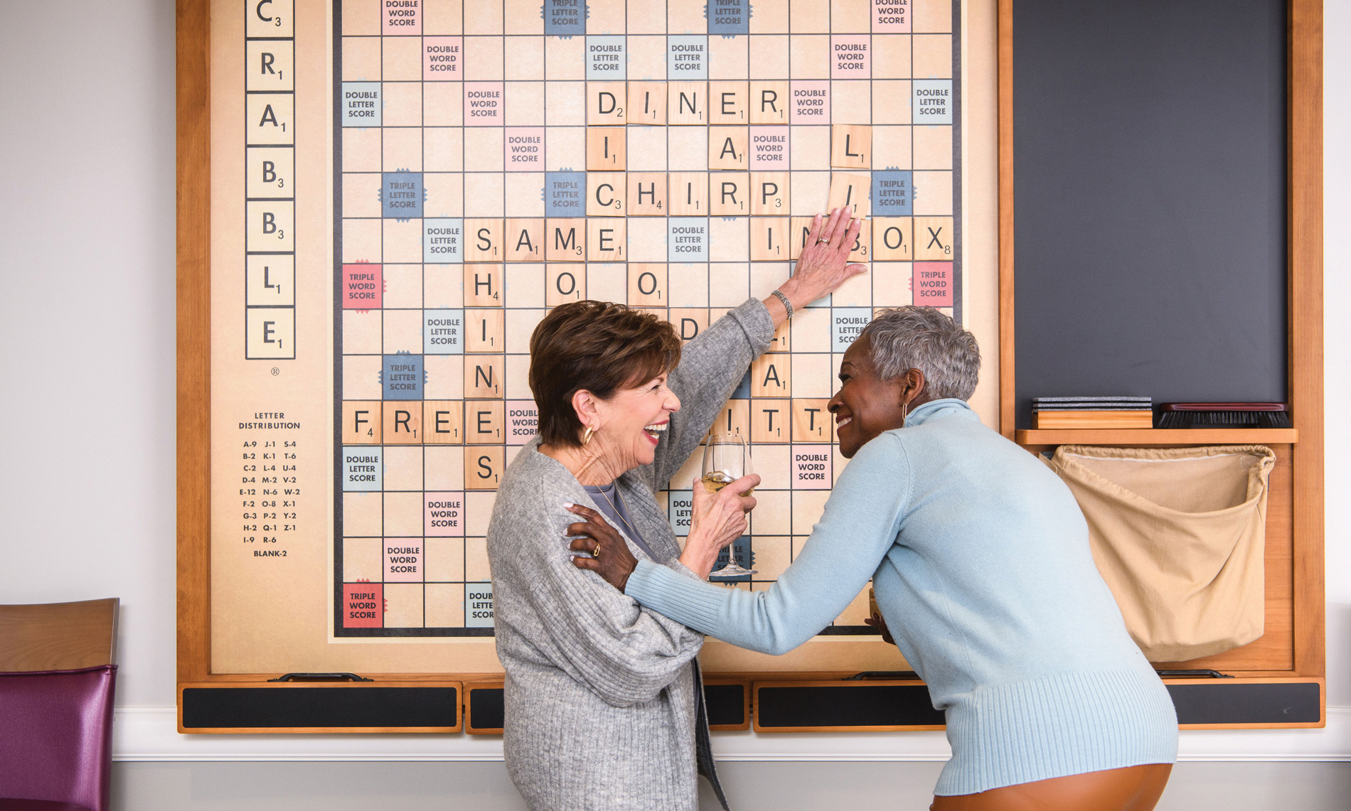 Elderly couple laughing and playing a game of scrabble on a giant wall mounted scrabble board