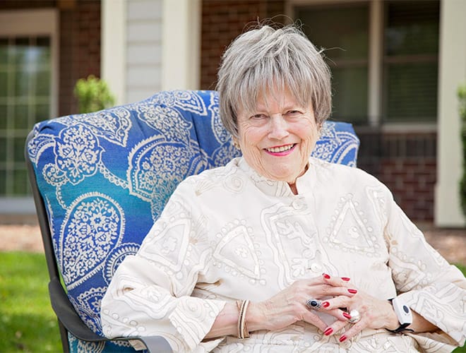 A resident sitting outdoors in a vintage chair with a victorian pattern on the cushion. 