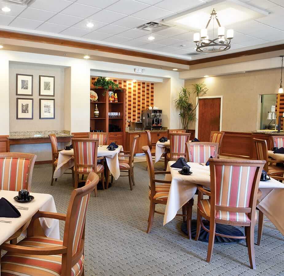 A formal dining room featuring tables of four set for meal service at the Fountains at the Carlotta, Emeryville CA