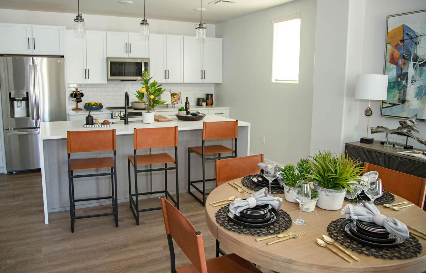 A modern kitchen with white cabinetry, stainless steel appliances, bar height chairs and a dining table in a model residence at The Hacienda at the River