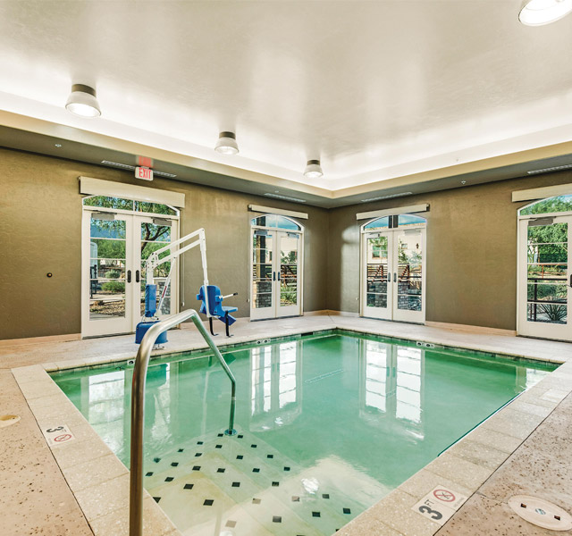 An indoor pool with chair that can be raised and lowered into the pool for individuals with mobility issues at The Hacienda at the River