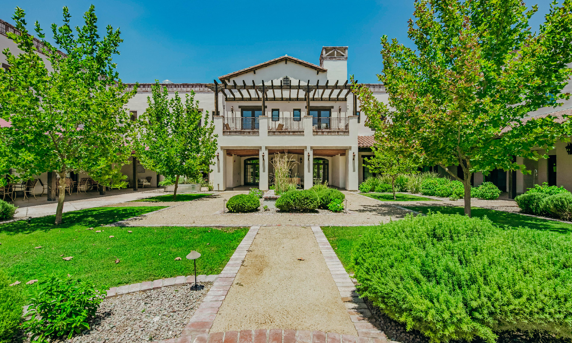 The main entrance of the The Hacienda at the River featuring luscious green grass, large trees, and a stone pathway