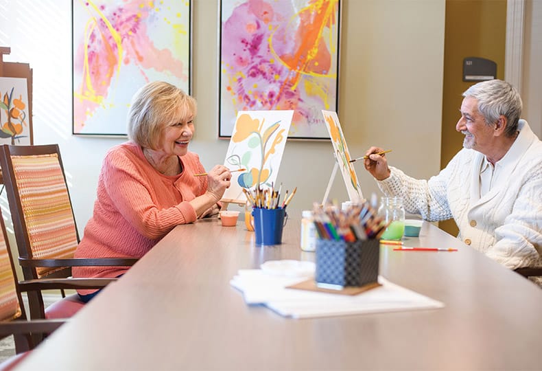 A man and a woman sitting at a table painting with water colours