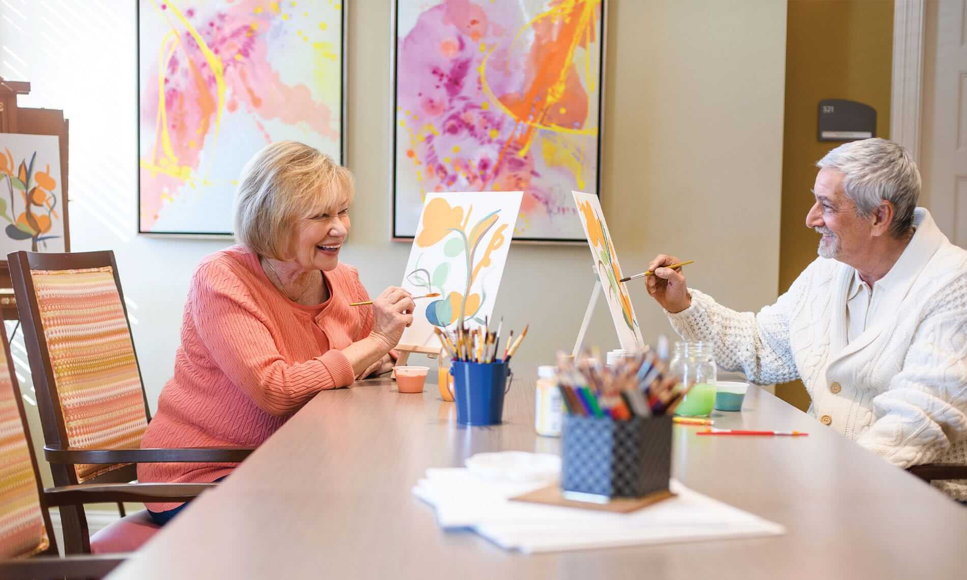 A man and a woman sitting at a table painting with water colours