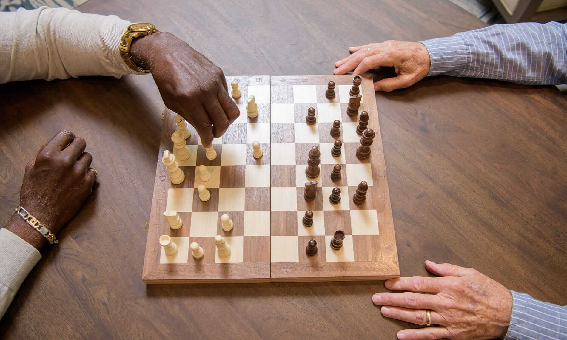 A pair of elderly gentleman's hands are visible on either side of a wooden chess board