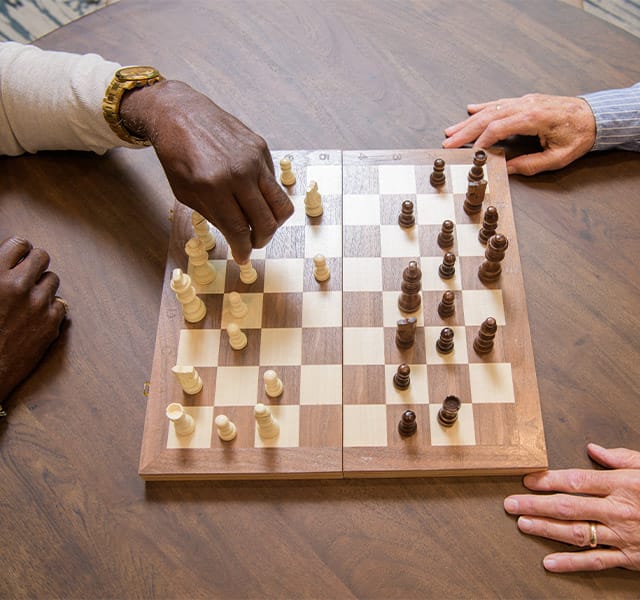 A pair of elderly gentleman's hands are visible on either side of a wooden chess board