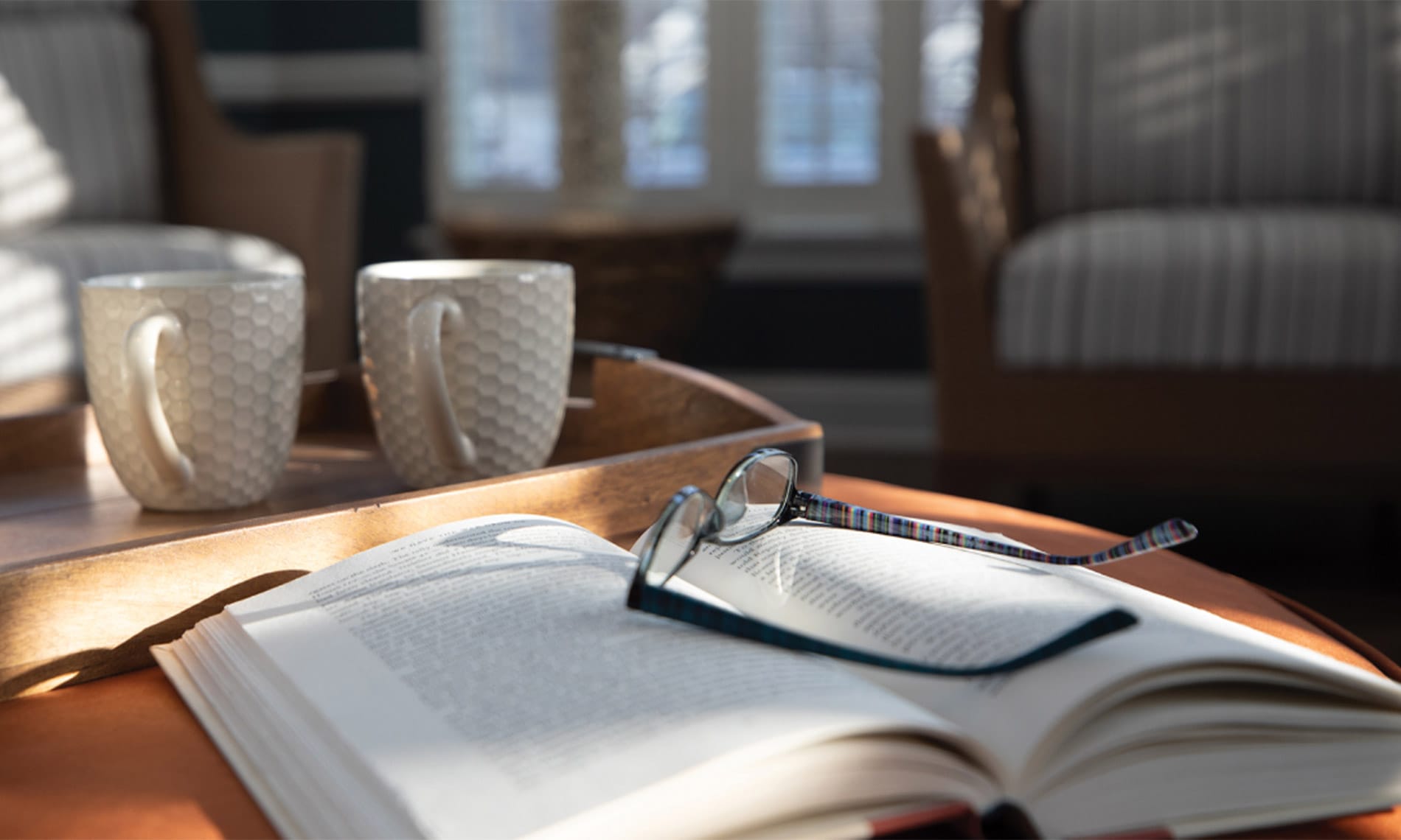 glasses on top of a book with coffee cups on the table
