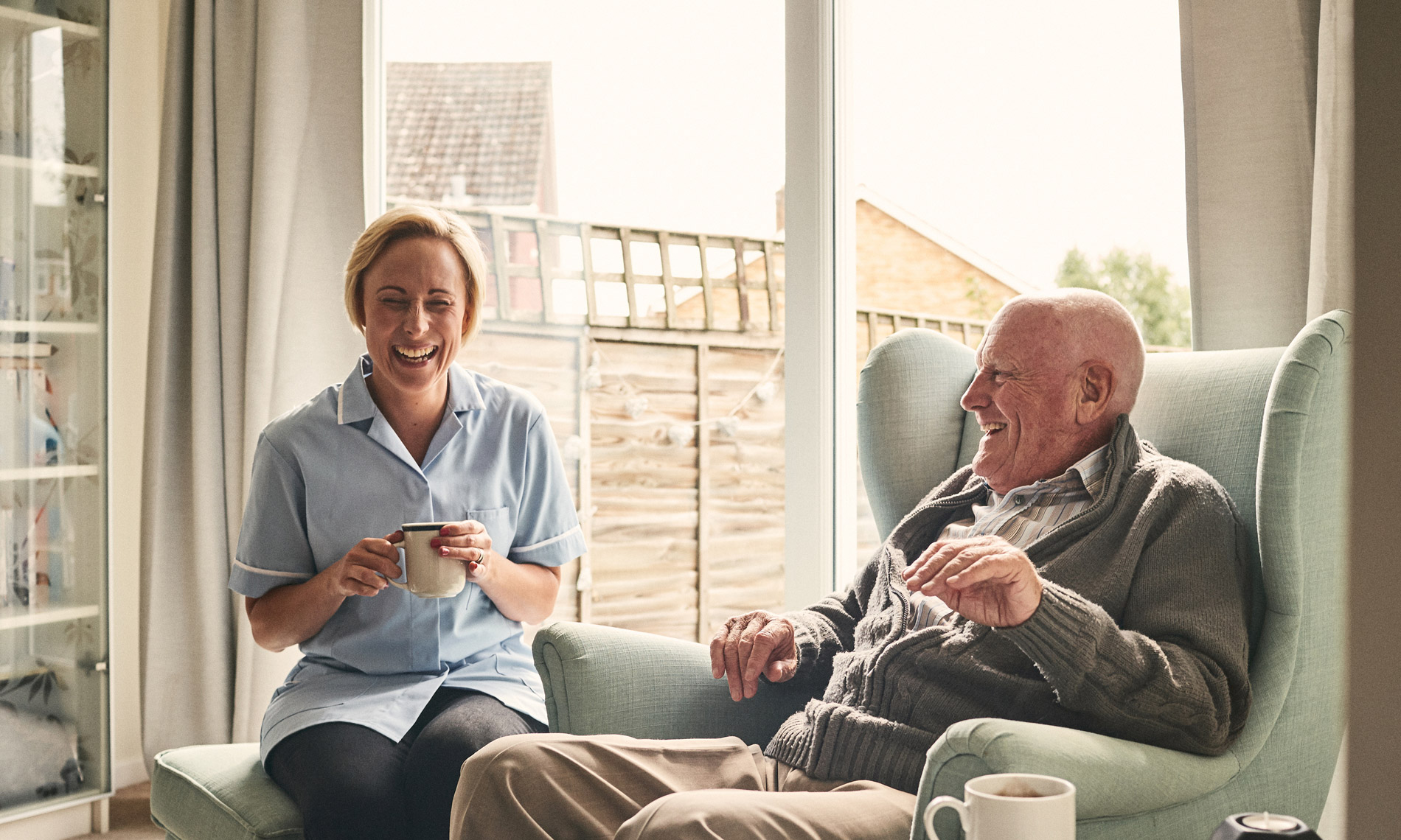 An elderly man sitting and having a laugh with his aid. 