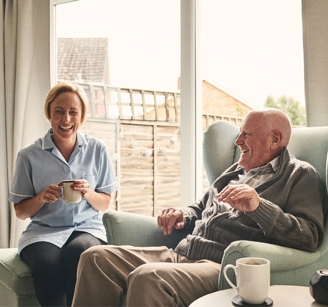 An elderly man sitting and having a laugh with his aid. 