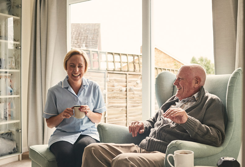 An elderly man sitting and having a laugh with his aid. 