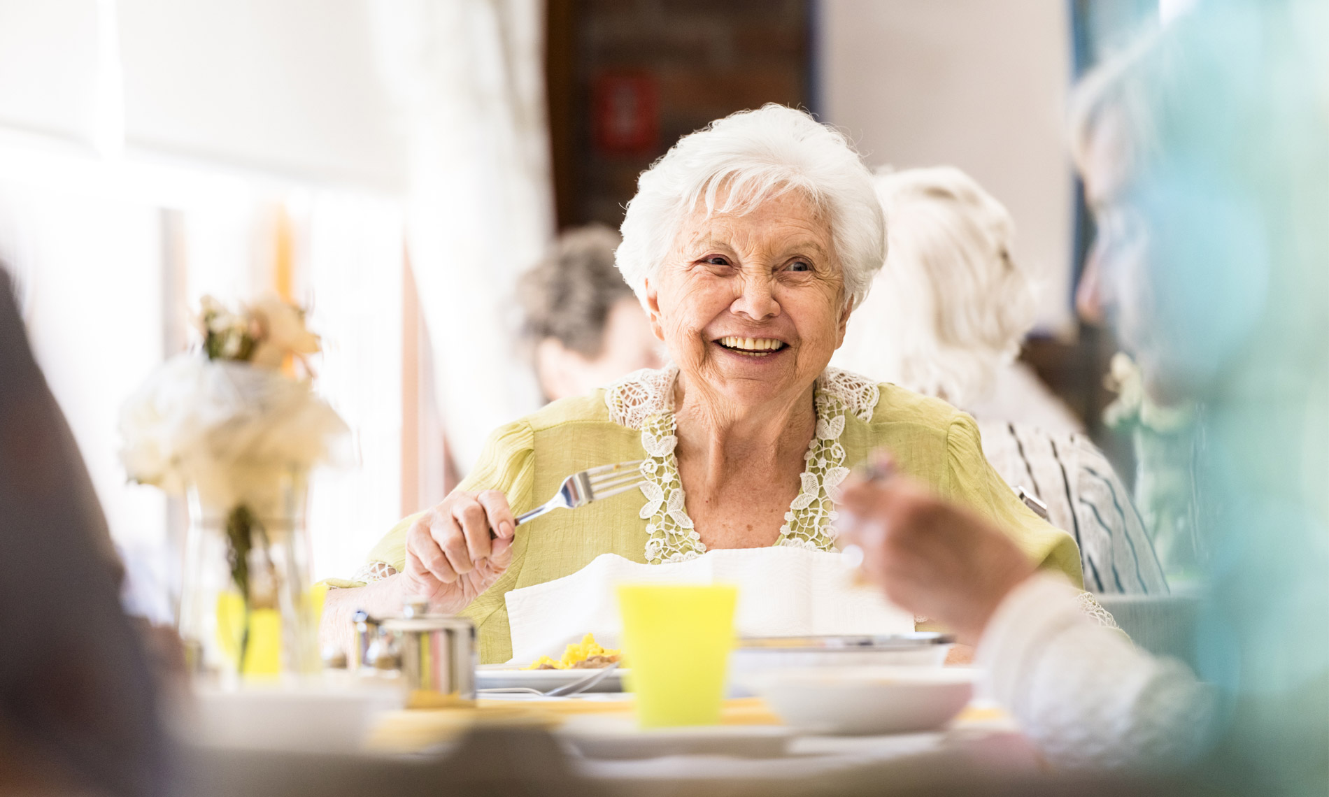 an elderly woman enjoying a meal with her peers and looking as if she reflects on some memory