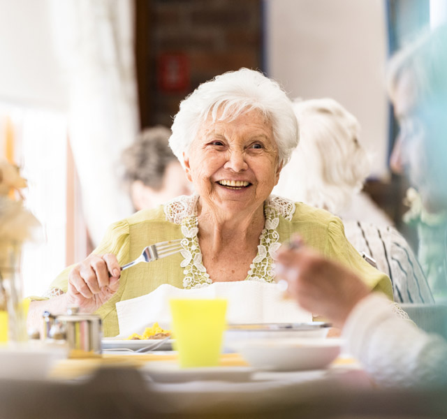an elderly woman enjoying a meal with her peers and looking as if she reflects on some memory