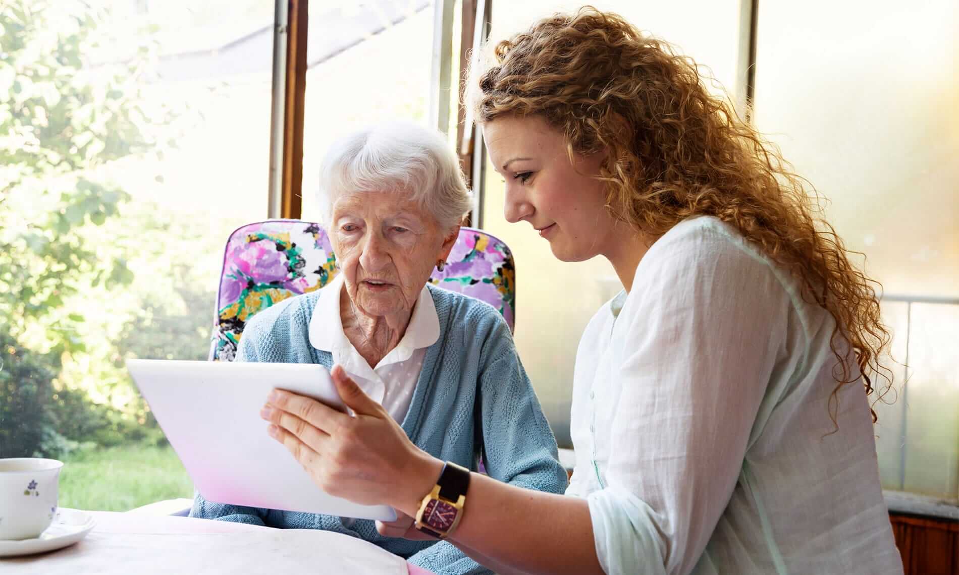 young woman helping elderly lady with tablet device