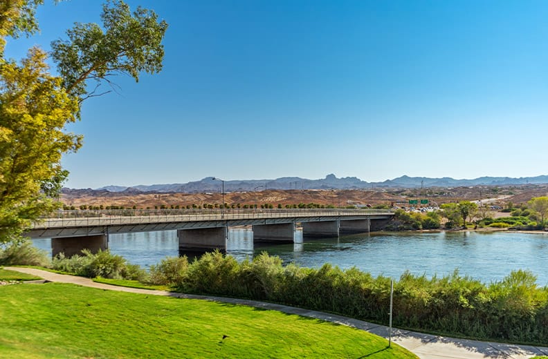 Green grass and river with a bridge heading into Bullhead City, Az