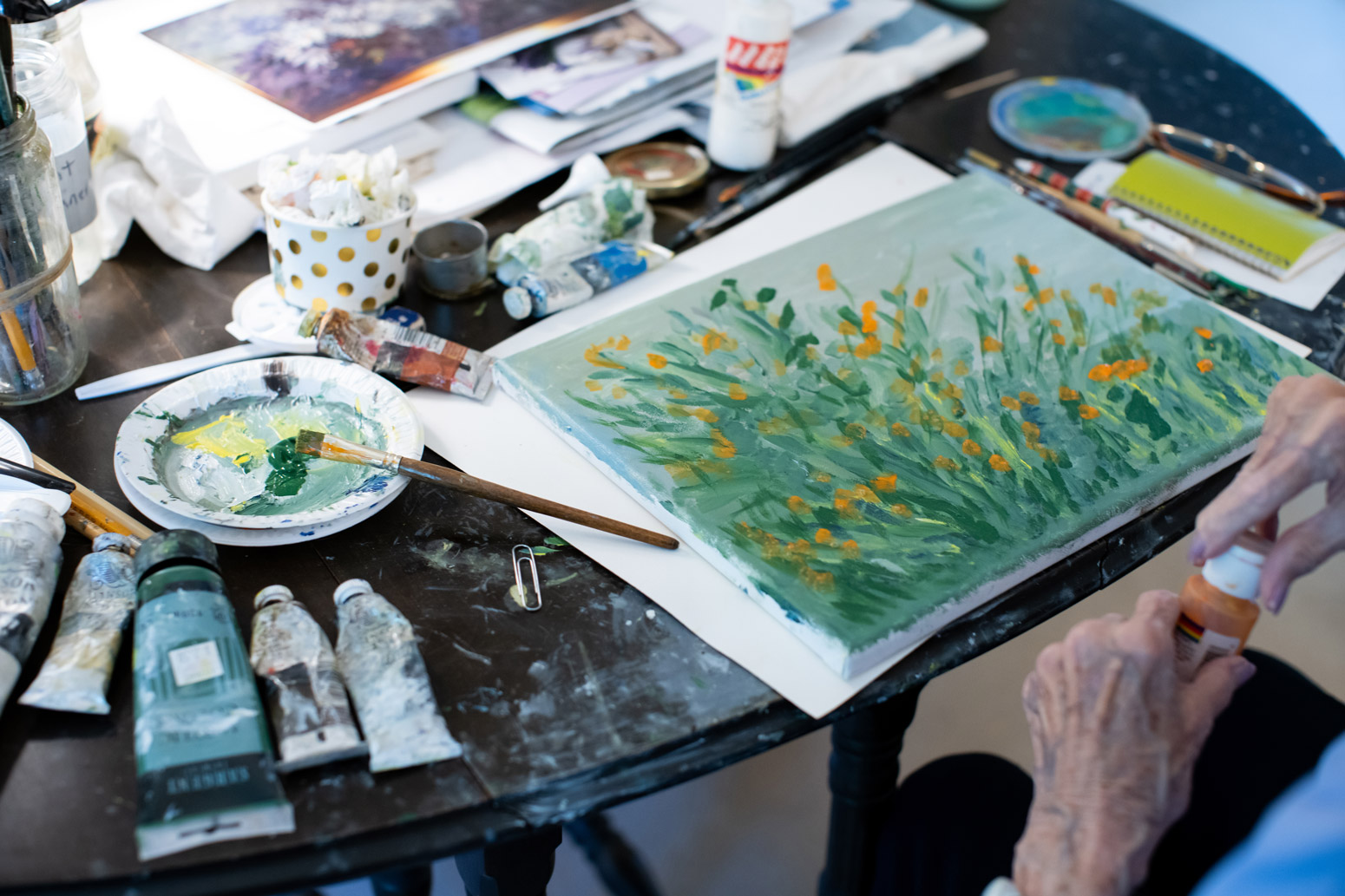 Watercolour set atop a wooden table while a woman opens a new container of paint