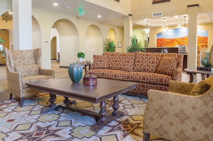 A shot of the Caliche Senior Living lobby, showing retro armchair and couch with a painting of a classic Arizona landscape on the back wall 