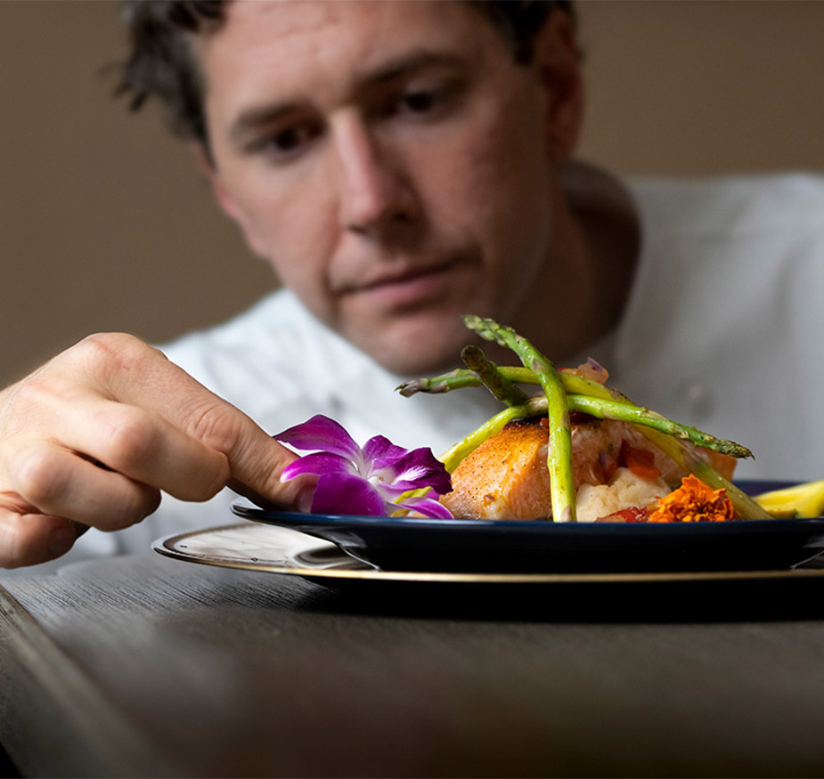 A chef placing a decorative flower on the edge of a meal to enhance the presentation A chef placing a decorative flower on the edge of a meal to enhance the presentation