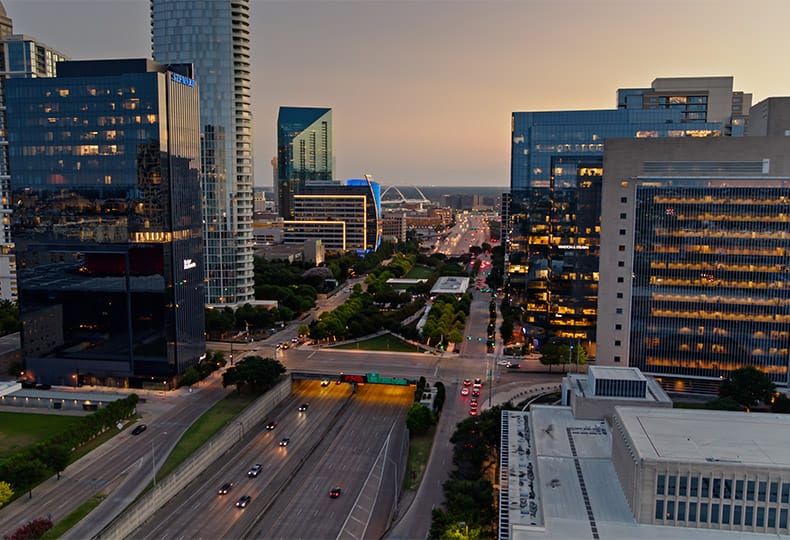 The Preston of the Park Cities Klyde Warren Park Aerial shot of Dallas on a summer evening, looking along the Woodall Rodgers Freeway (Spur 366) where it passes beneath Klyde Warren Park.