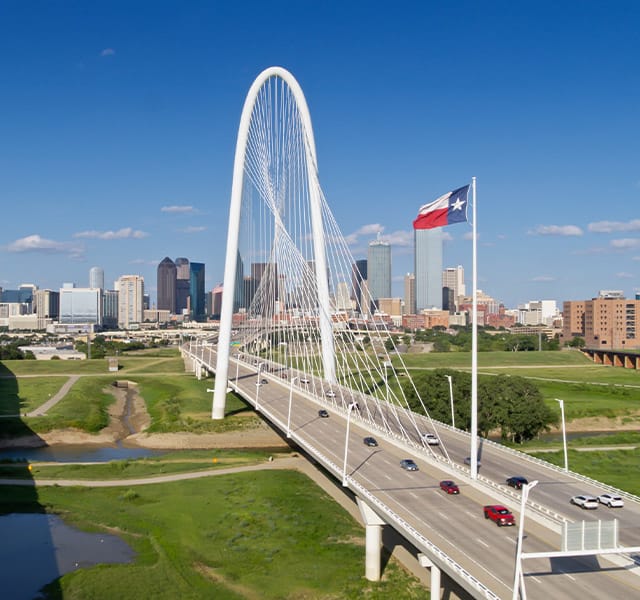 The Preston of the Park Cities Lone Star State Aerial shot of Dallas, Texas, looking along the Margaret Hunt Hill and Roland Kirk bridges crossing the Trinity River into downtown Dallas on a sunny day in summer.
