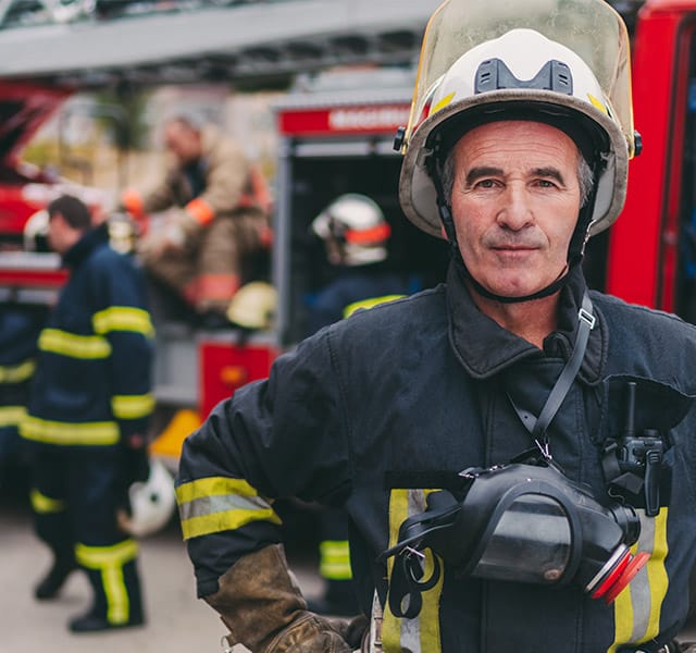 Fire Rescue A fire fighter standing in full uniform in front of a fire truck while other crew members stand in a circle talking