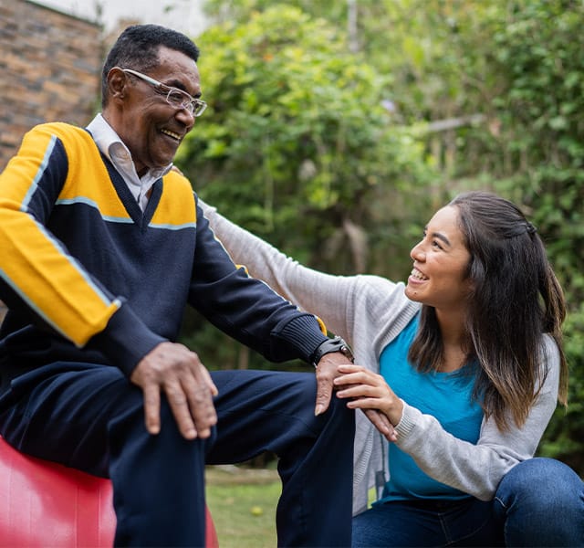 The Fountains at the Albemarle Partnerships - HealthPro Physical therapist talking to an elderly african american man sitting on a fitness ball outdoors