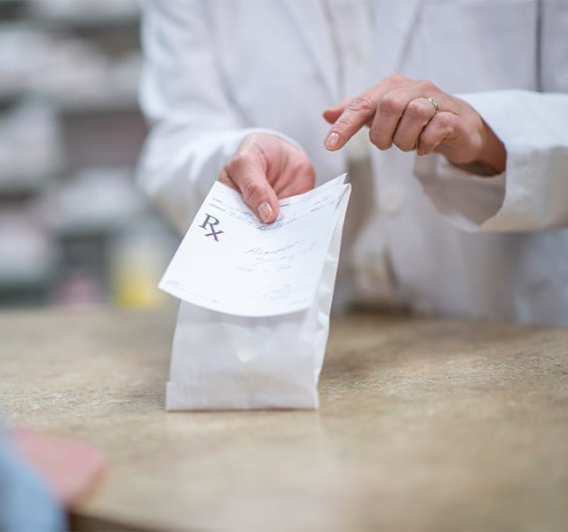 The Fountains at the Albemarle Partnerships - Pharmacy Partners A pharmacist in a white lab coat holds out a processed and packaged prescription as he explains how to properly and safely take the medication.