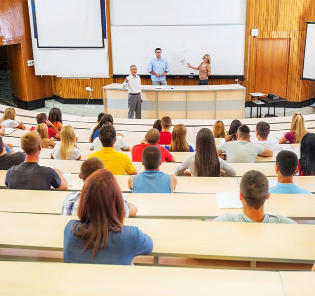 University Campus Students in a university lecture hall with the professor, a teacher aid and a guest at the front