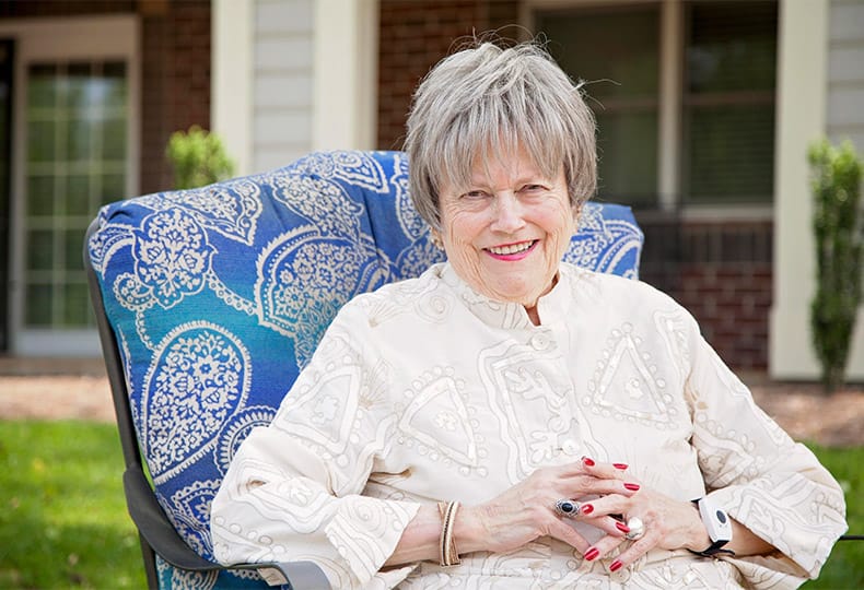 The Fountains at the Albemarle Testimonials A woman sitting in a chair in an outdoor resident space at the Fountains at the Albemarle
