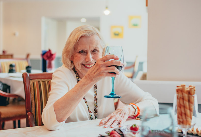The Preston of the Park Cities Testimonials A female resident smiling while holding up a glass of red wine during one of the happy hours hosted at the Preston of the Park Cities