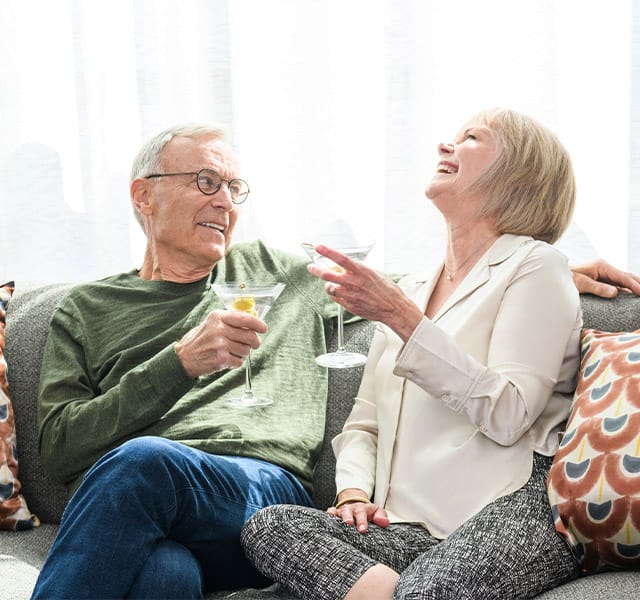 Amenities & Services Watermark at Home Residents laughing on a couch in their apartment at one of the many properties Watermark Retirement Communities operates across the United States