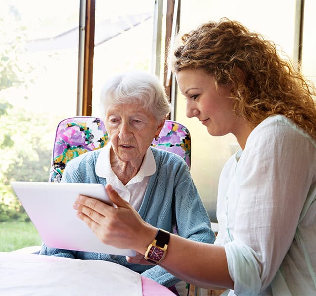 Tech Concierge young woman helping elderly lady with tablet device